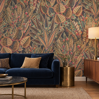 Papier peint feuillage botanique sombre noir, beige et rouge dans un salon avec canapé en velours bleu